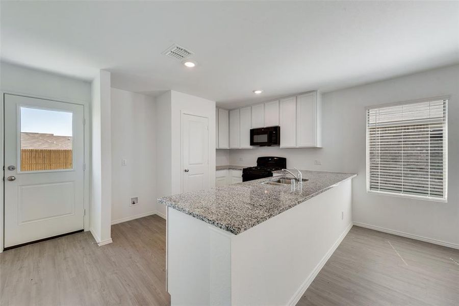 Kitchen featuring light stone counters, white cabinets, kitchen peninsula, black appliances, and sink