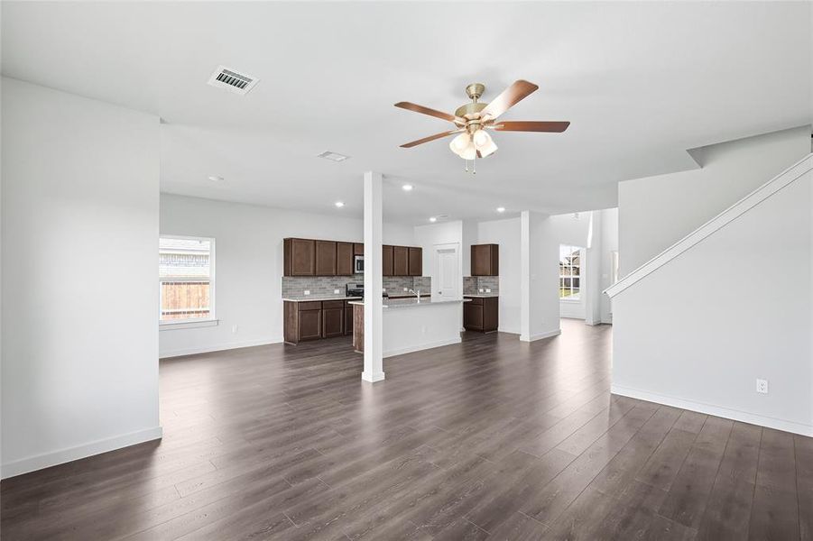 Unfurnished living room with healthy amount of natural light, dark wood-style flooring, ceiling fan, recessed lighting, and stairway Unfurnished living room with healthy amount of natural light, dark wood-style flooring, ceiling fan, recessed lighting, and stairway
