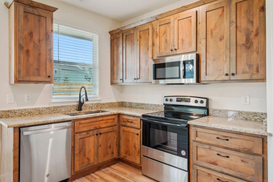 Kitchen featuring a sink, light stone countertops, appliances with stainless steel finishes, and light wood-style flooring