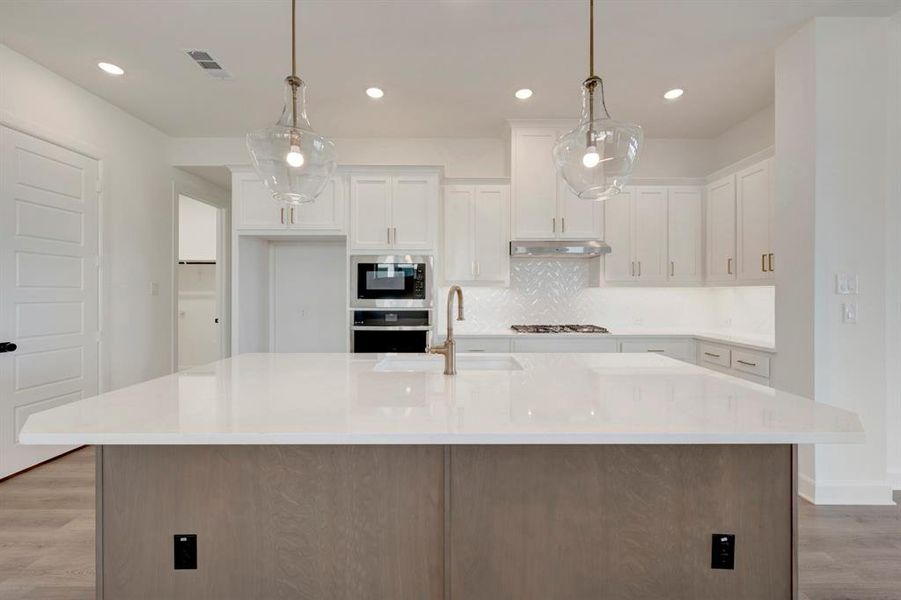 Two tone kitchen featuring light wood finished floors, a kitchen island with sink, stainless steel appliances, light stone countertops, and two tone cabinets Two tone kitchen featuring light wood finished floors, a kitchen island with sink, stainless steel appliances, light stone countertops, and two tone cabinets