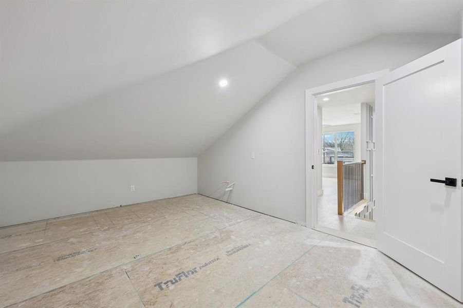 Unfinished attic space with sloped ceilings, recessed lighting, and a white flat-panel door with black hardware