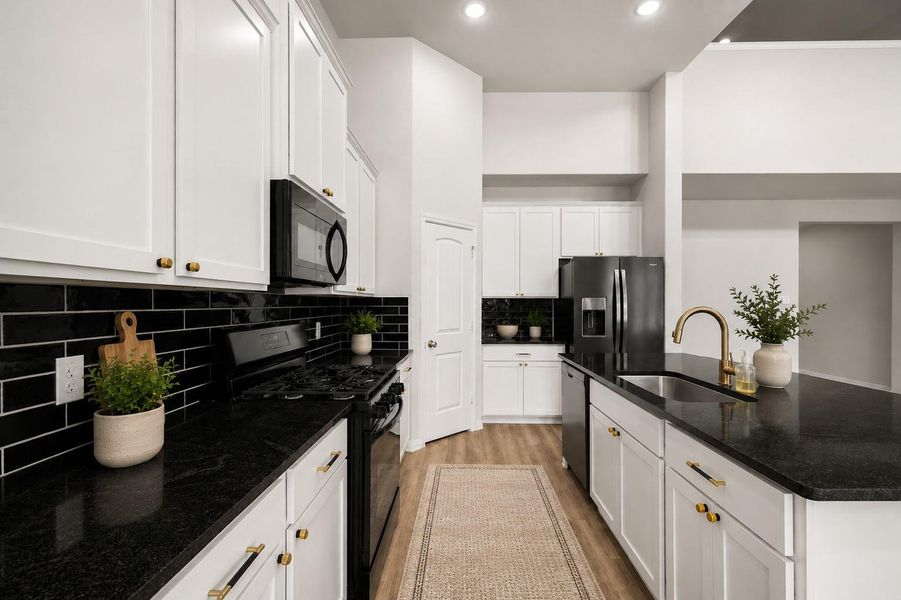 Sleek modern kitchen featuring white cabinetry, black countertops, and a stylish subway tile backsplash, complemented by stainless steel appliances and brass fixtures.