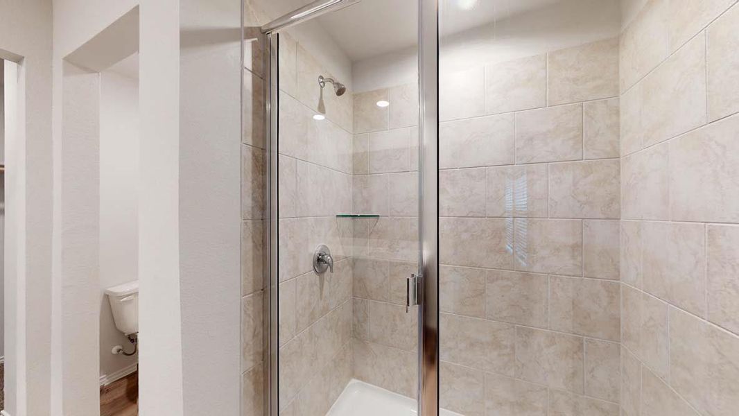 Tiled shower enclosure featuring a clear glass door, chrome fixtures, and a corner glass shelf