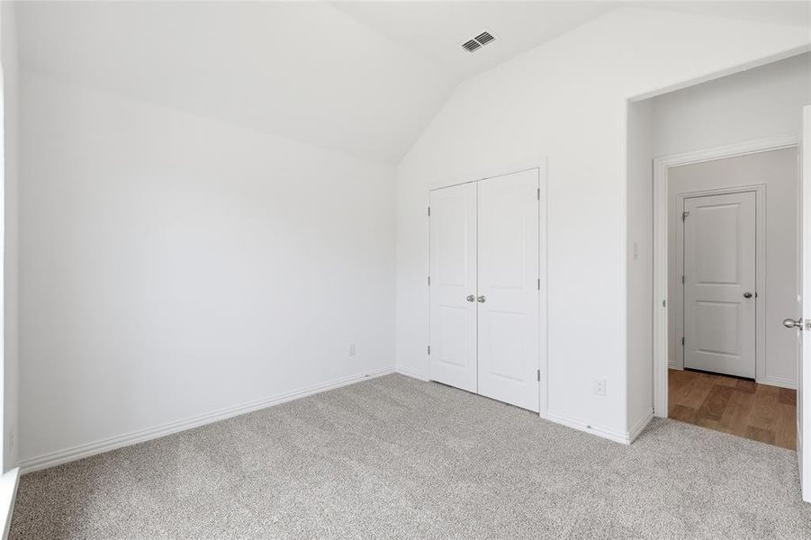 Carpeted room featuring a vaulted ceiling, bi-fold closet doors, and light wall finishes