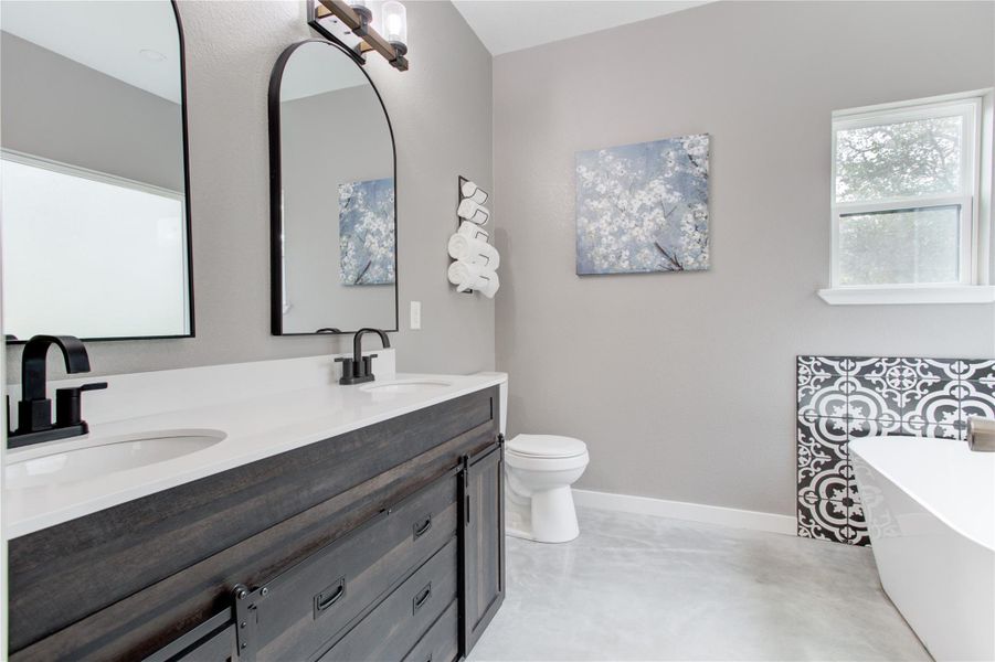 Bathroom featuring concrete flooring, a freestanding tub, double vanity, baseboards, and toilet