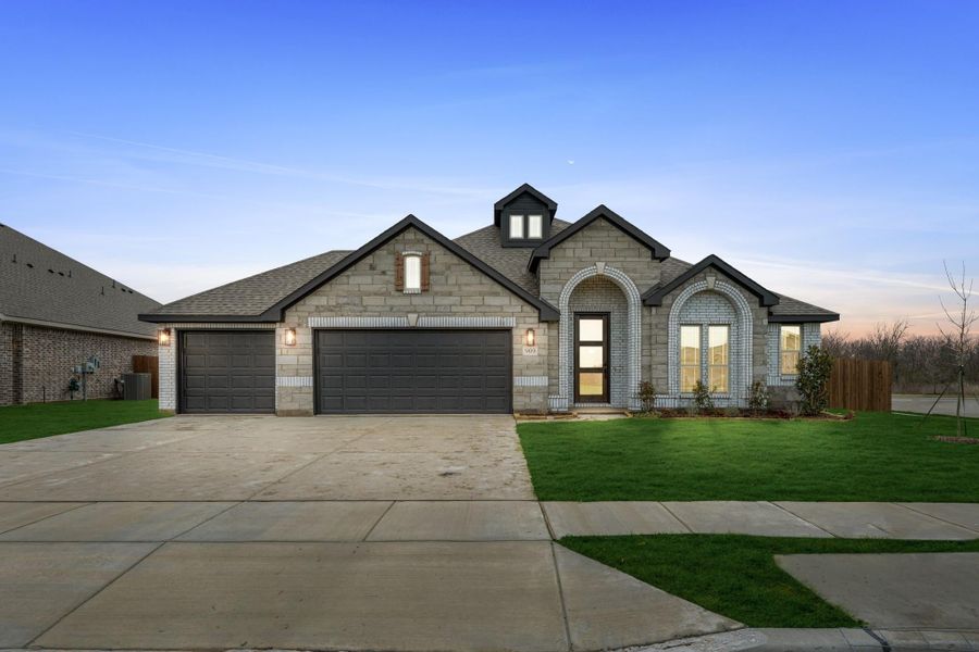 Single-story stone home with arched entry, three-car garage, and green front lawn at dusk