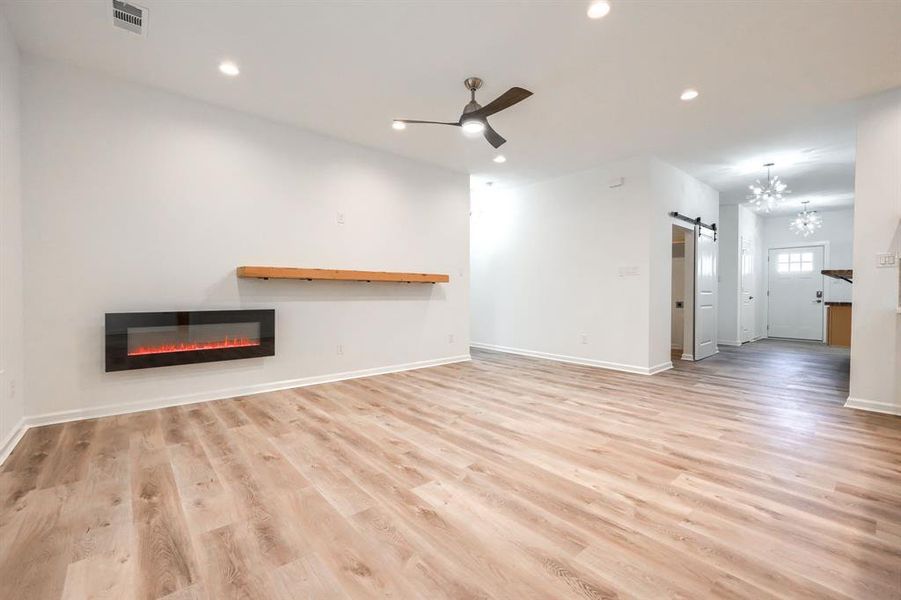 Unfurnished living room with a barn door, recessed lighting, light wood-style floors, ceiling fan, and a chandelier