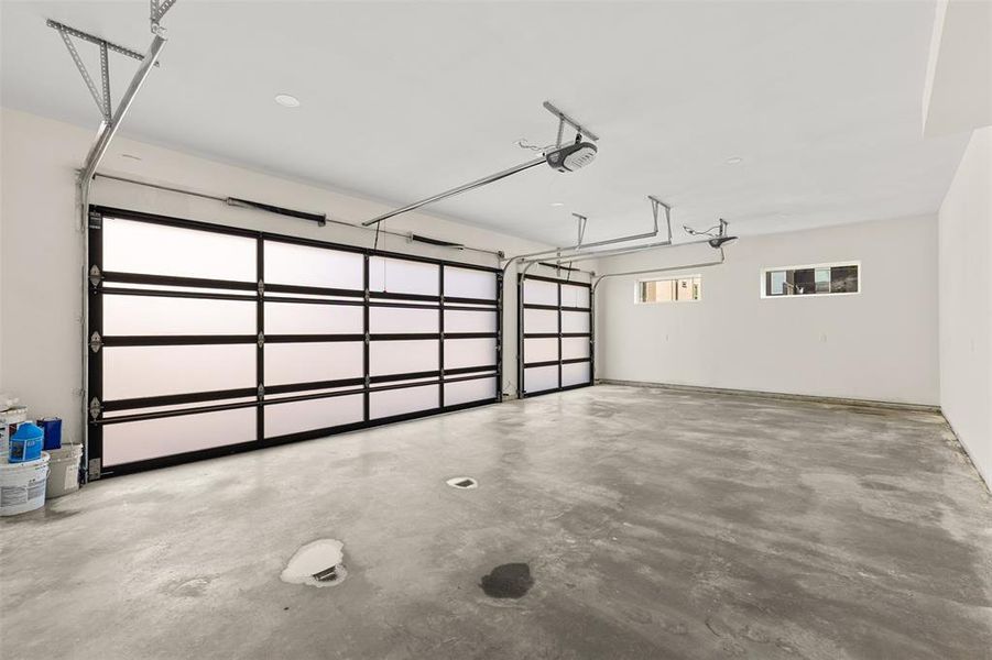 Spacious garage featuring two modern glass panel doors, a concrete floor, and multiple transom windows providing natural light