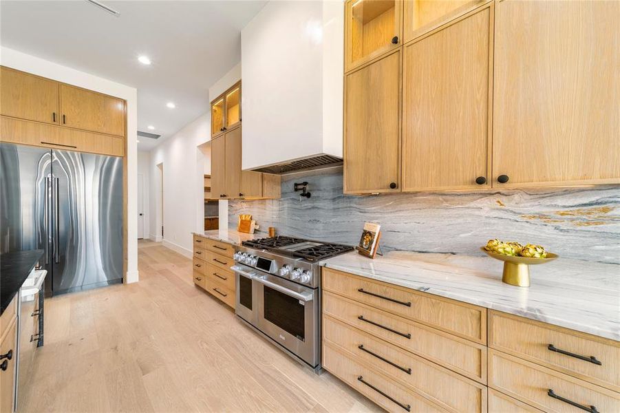 Kitchen with high end appliances, light stone counters, light wood finish cabinets, light wood-type flooring, and recessed lighting