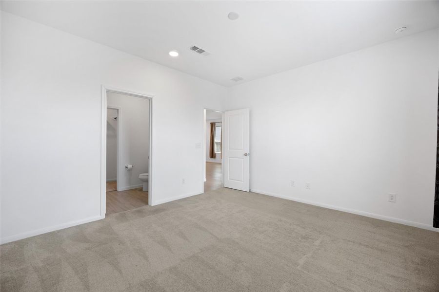 neutral carpet and white walls, creating a bright, open space. It includes a door leading to a bathroom and another to the hallway, offering convenience and accessibility.