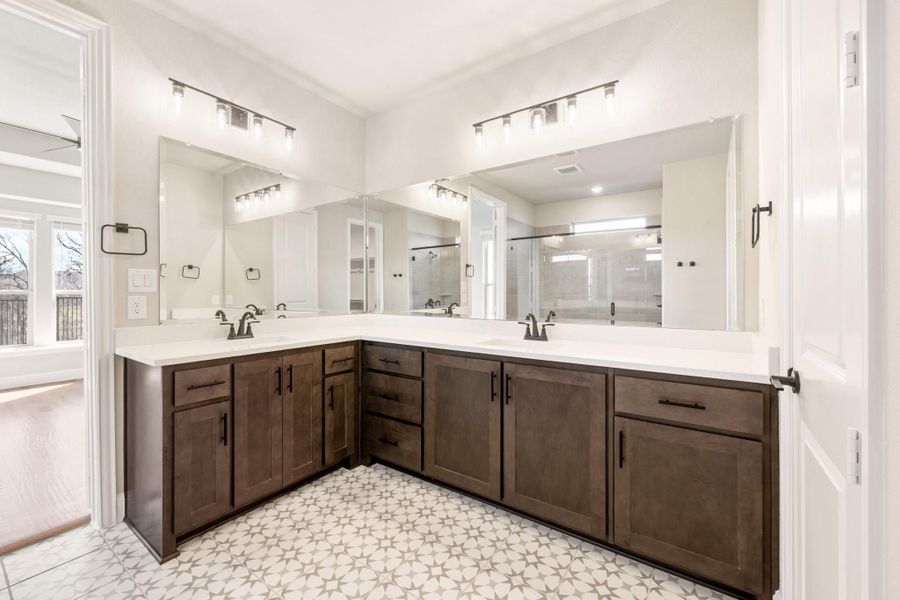 Master bathroom with L-shaped double vanity, dark wood cabinets, white countertops, and patterned tile floor