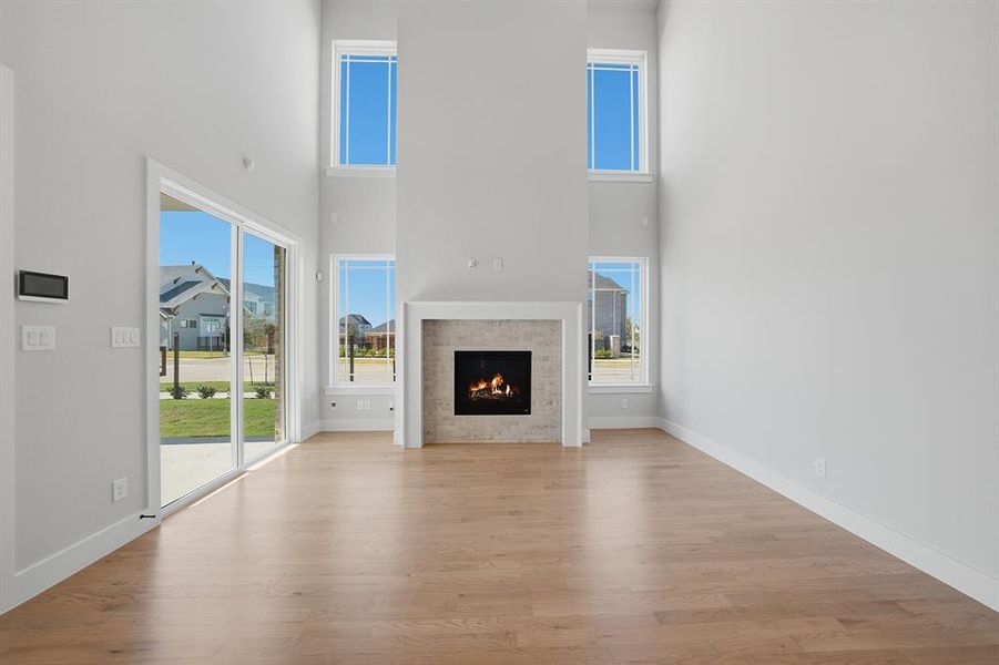 Unfurnished living room featuring a high ceiling, light wood-type flooring, plenty of natural light, and a lit fireplace
