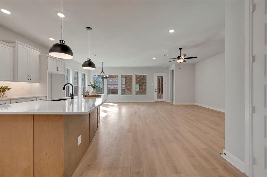 Kitchen featuring light wood-style flooring, light stone countertops, an island with sink, backsplash, and open floor plan