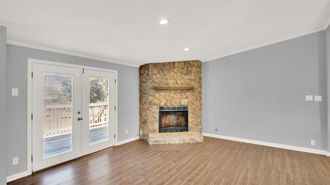 Unfurnished living room with ornamental molding, french doors, a stone fireplace, wood finished floors, and recessed lighting