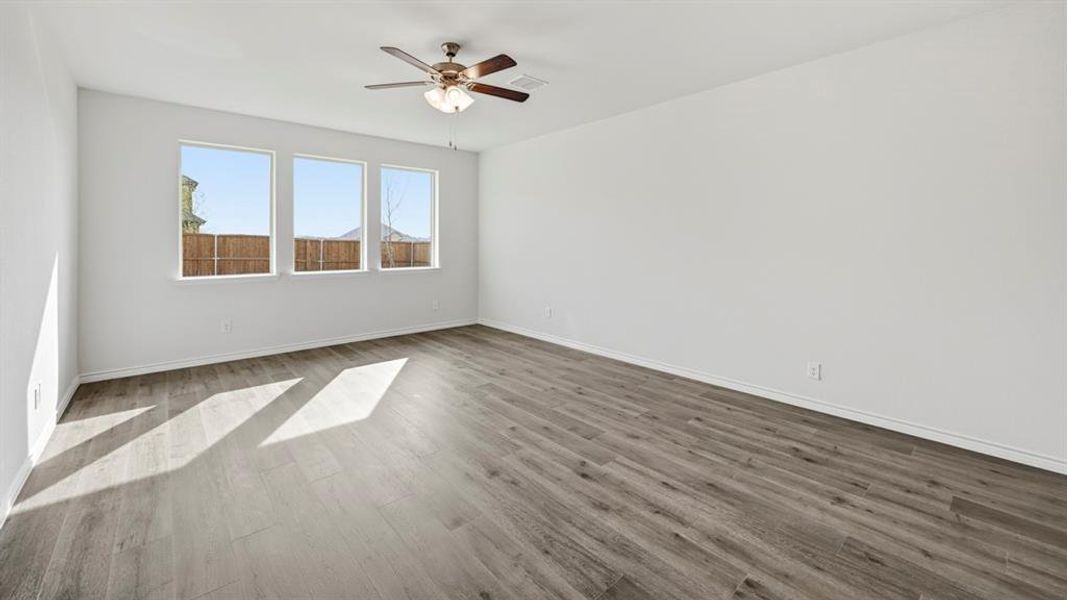 Spacious room featuring wood-finish flooring, a contemporary ceiling fan, and three large windows providing abundant natural light Spacious room featuring wood-finish flooring, a contemporary ceiling fan, and three large windows providing abundant natural light