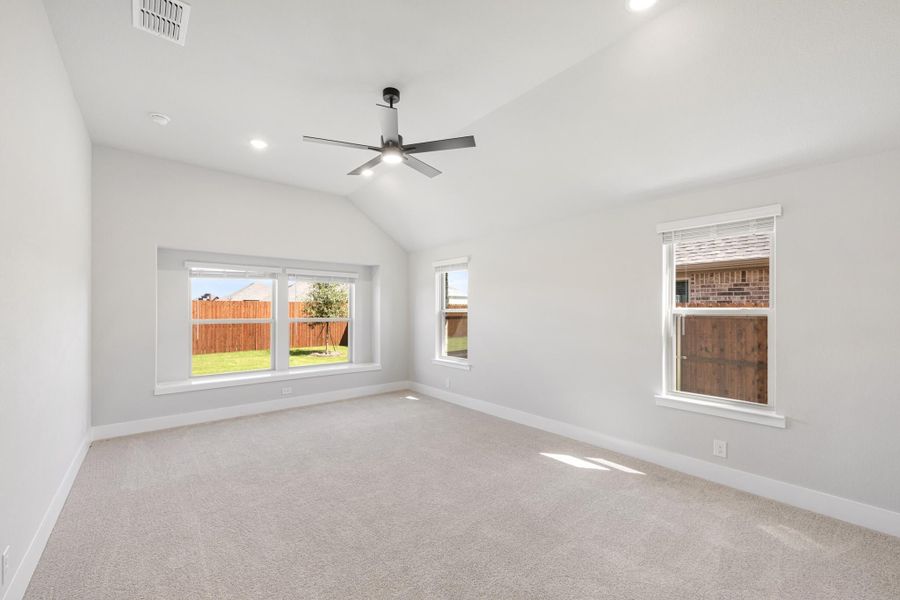 Empty bedroom with vaulted ceiling, ceiling fan, carpet flooring, and multiple windows Empty bedroom with vaulted ceiling, ceiling fan, carpet flooring, and multiple windows