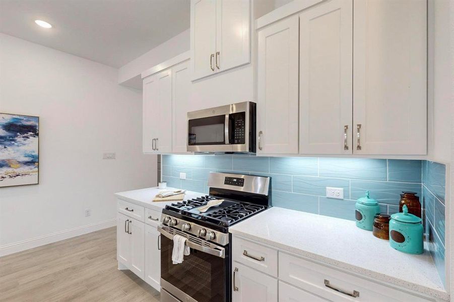 Kitchen with appliances with stainless steel finishes, white cabinets, light wood-type flooring, and tasteful backsplash