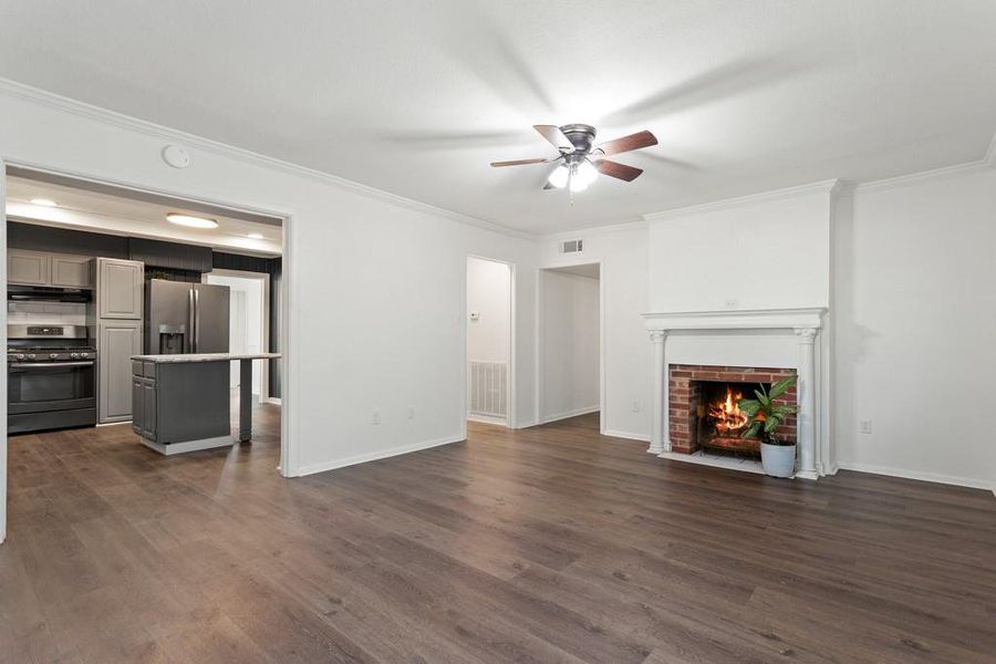 Unfurnished living room with ceiling fan, crown molding, dark wood finished floors, and a fireplace with flush hearth