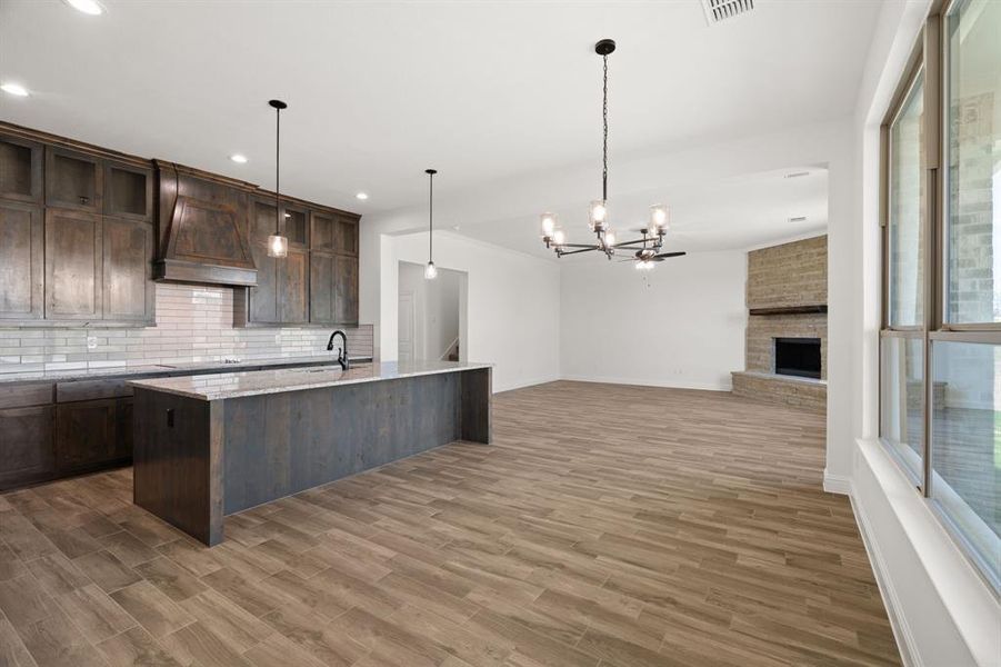 Kitchen with backsplash, decorative light fixtures, a chandelier, light stone countertops, and dark brown cabinetry Kitchen with backsplash, decorative light fixtures, a chandelier, light stone countertops, and dark brown cabinetry