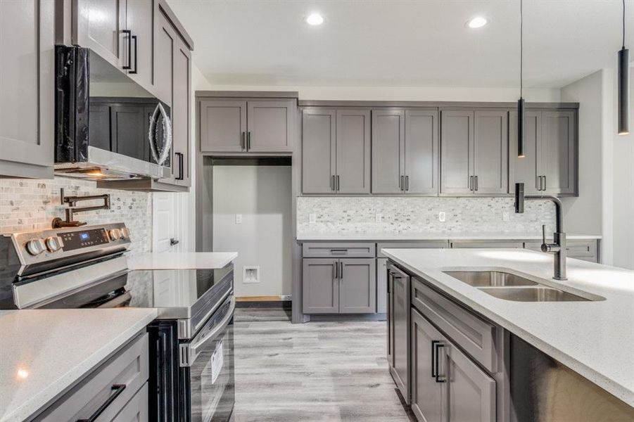 Kitchen featuring hanging light fixtures, sink, decorative backsplash, light wood-type flooring, and appliances with stainless steel finishes