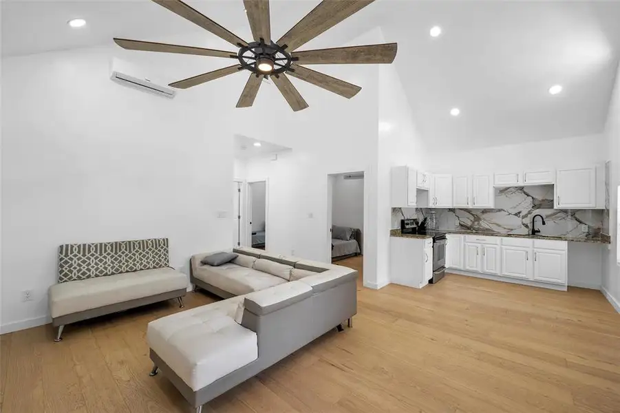 Living area featuring high vaulted ceiling, a ceiling fan, light wood-type flooring, a wall mounted AC, and recessed lighting Living area featuring high vaulted ceiling, a ceiling fan, light wood-type flooring, a wall mounted AC, and recessed lighting