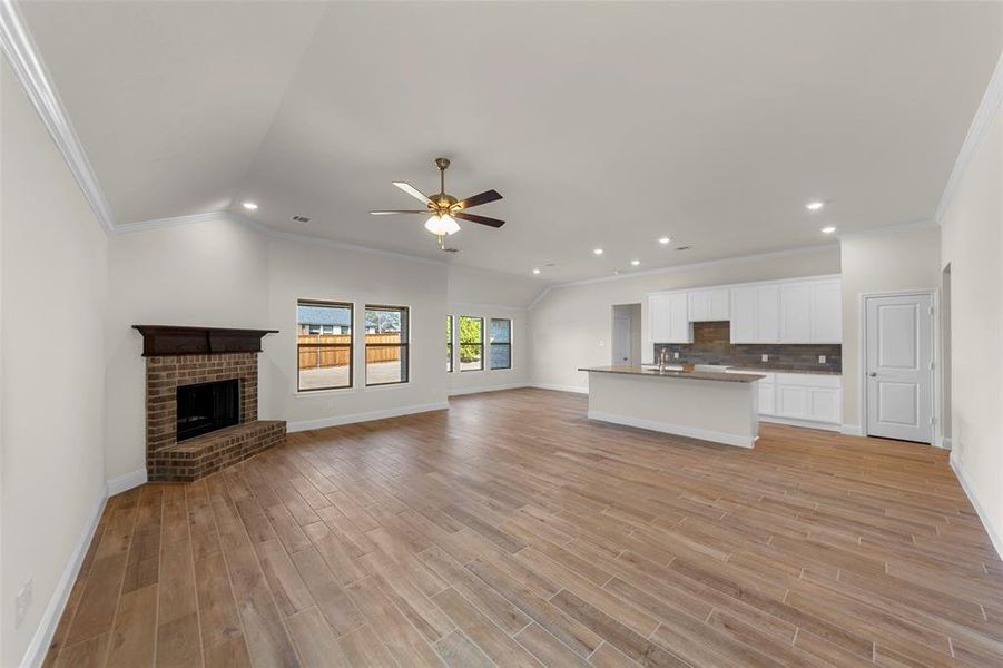 Unfurnished living room featuring ornamental molding, a ceiling fan, a brick fireplace, light wood-style floors, and recessed lighting