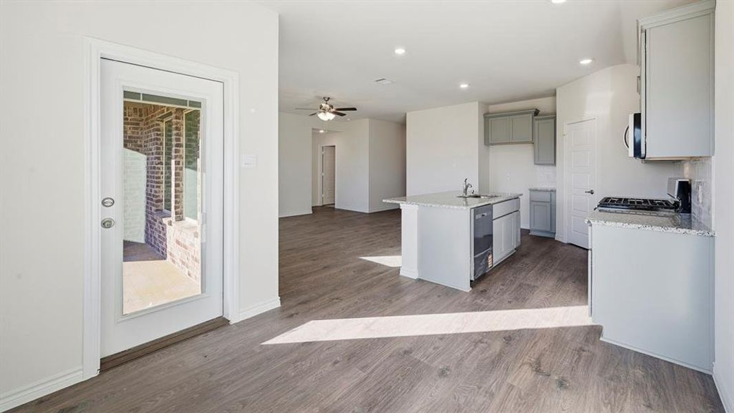 The property features an open-concept living area with wood-look flooring, a kitchen island with a sink, white cabinetry with a tile backsplash, and recessed lighting