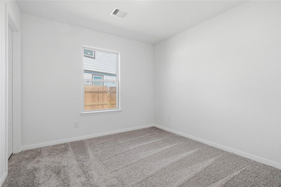 Tucked peacefully in the front of the home is this secondary bedroom which features plush carpeting, neutral paint, a large window, and a spacious closet.