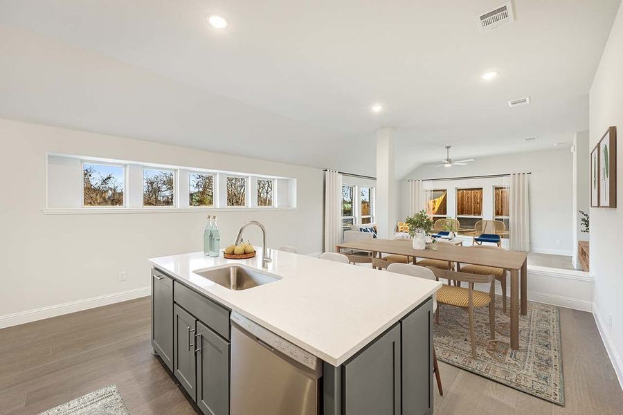 Kitchen island with gray cabinets and white countertop, open to dining area with hardwood floors