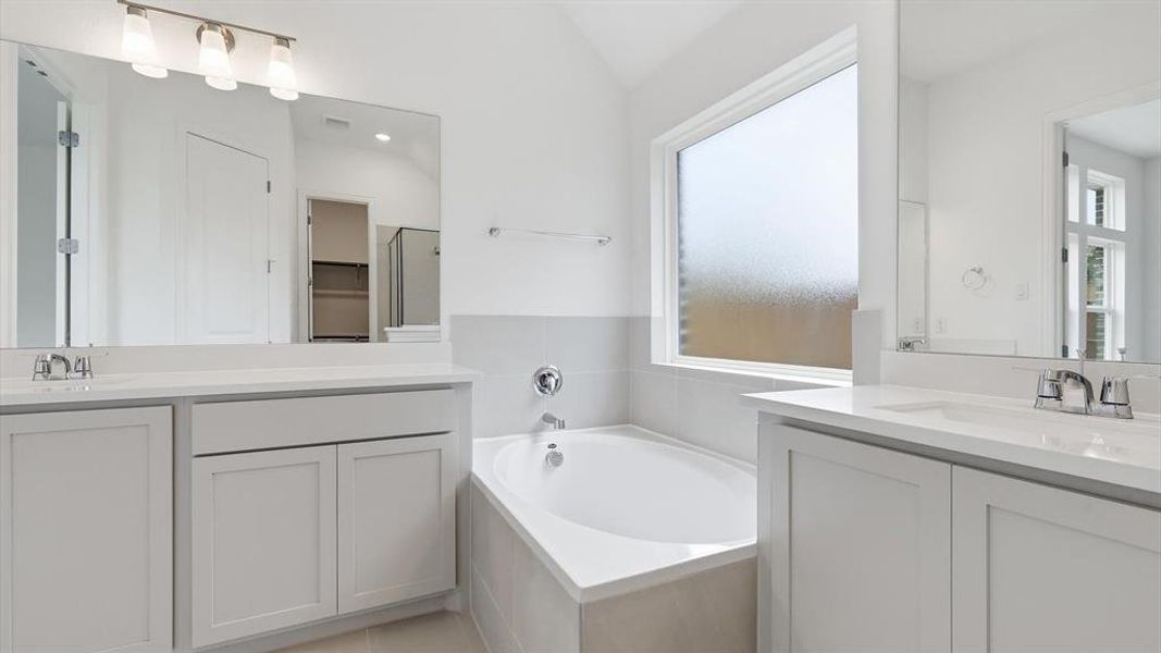 Bathroom featuring a corner soaking tub, dual vanity sinks with white countertops, and a large privacy window Bathroom featuring a corner soaking tub, dual vanity sinks with white countertops, and a large privacy window