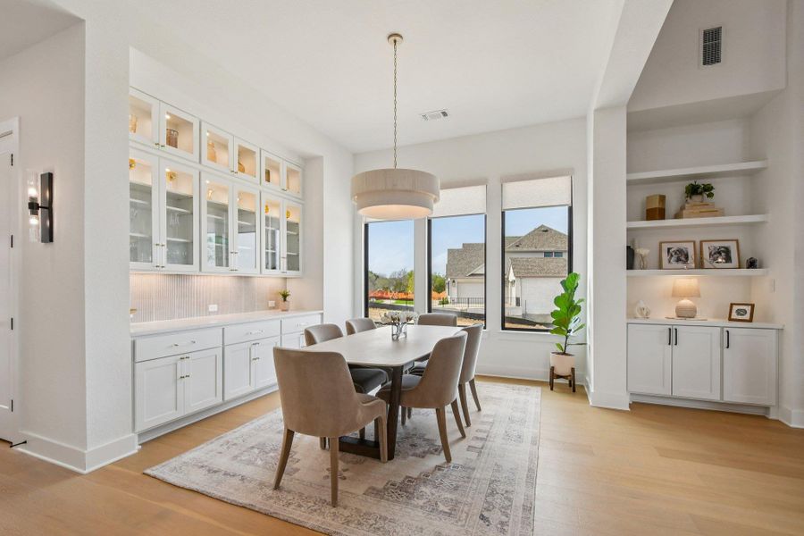 The dining area features white cabinetry with glass fronts and integrated lighting, a built-in shelving unit, and hardwood flooring The dining area features white cabinetry with glass fronts and integrated lighting, a built-in shelving unit, and hardwood flooring