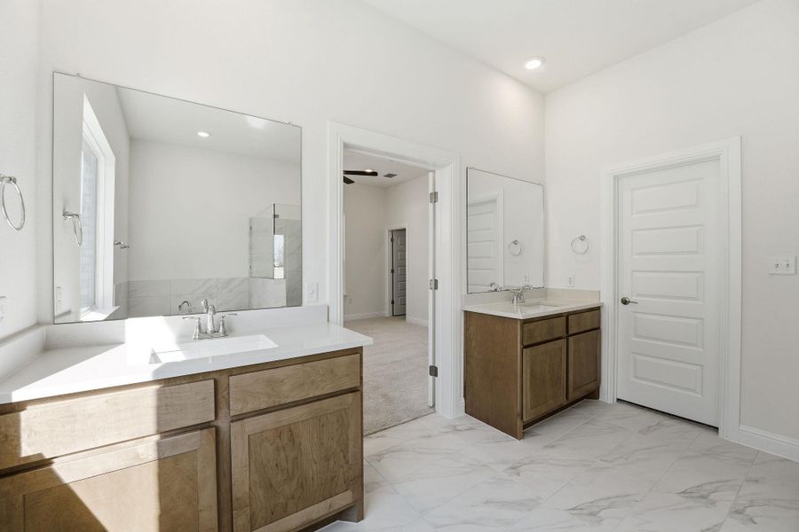 Bathroom with two vanities, light marble finish floors, and recessed lighting
