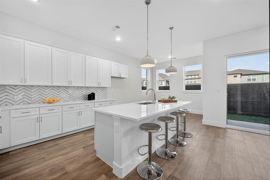 Kitchen with backsplash, white cabinetry, decorative light fixtures, a breakfast bar, and light wood-type flooring Kitchen with backsplash, white cabinetry, decorative light fixtures, a breakfast bar, and light wood-type flooring