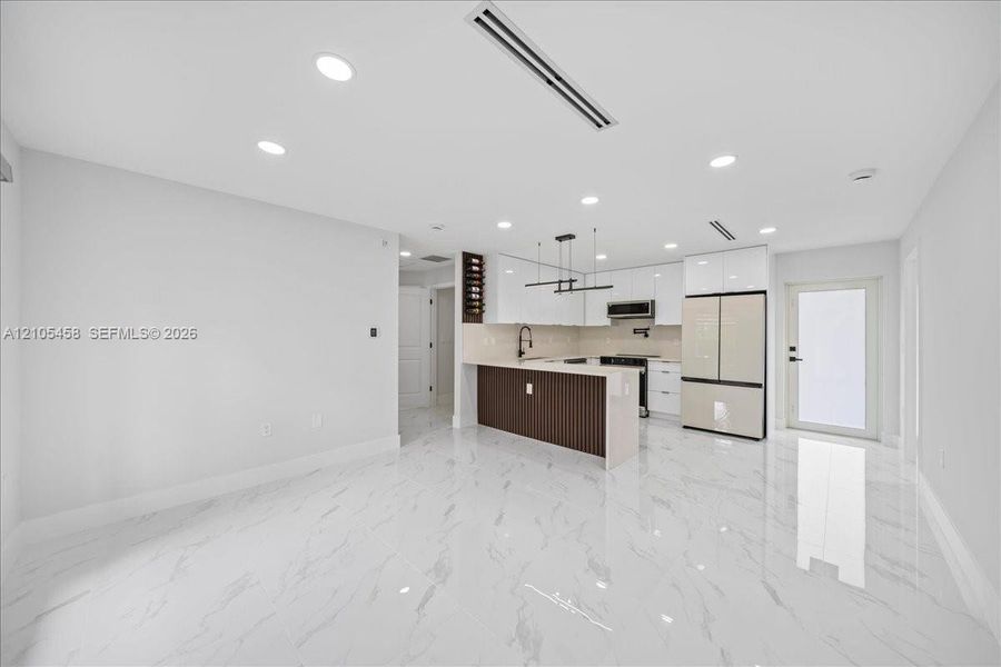 Open-concept living space featuring high-gloss tile flooring, recessed lighting, and a modern kitchen with white cabinetry Open-concept living space featuring high-gloss tile flooring, recessed lighting, and a modern kitchen with white cabinetry