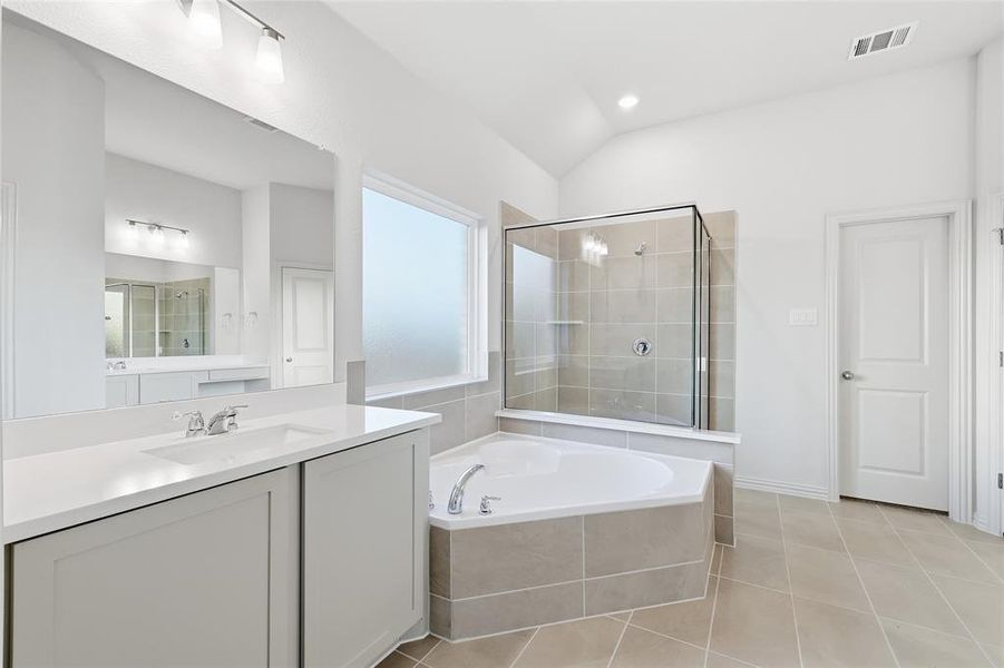 Full bathroom featuring a shower stall, a garden tub, vanity, light tile patterned floors, and vaulted ceiling