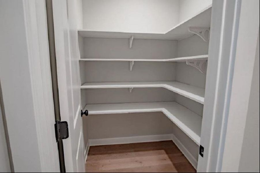Walk-in pantry featuring white shelving, light wood-finish flooring, and a white door with dark hardware