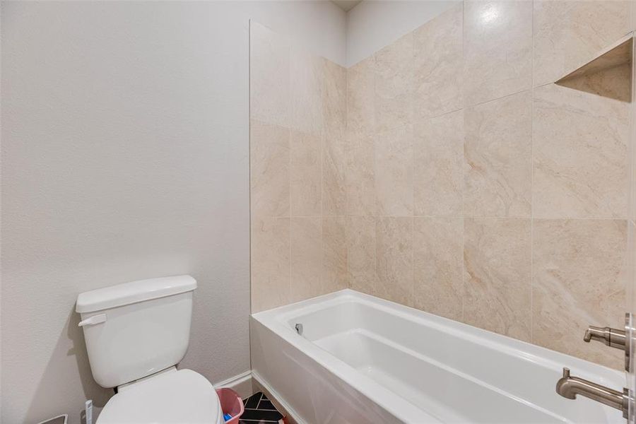 Bathtub and shower surround featuring large-format tile, a built-in shower niche, and brushed nickel fixtures