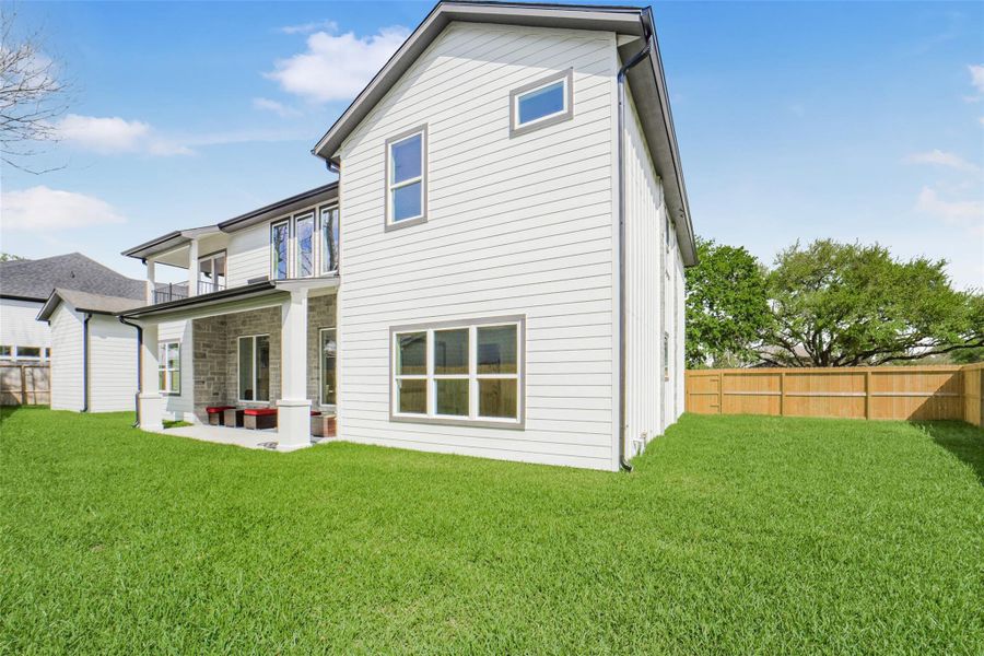 This photo showcases a modern two-story home with a spacious, well-maintained yard. The exterior features a mix of stone and siding, a covered patio, and a fenced backyard, ideal for privacy and outdoor activities.