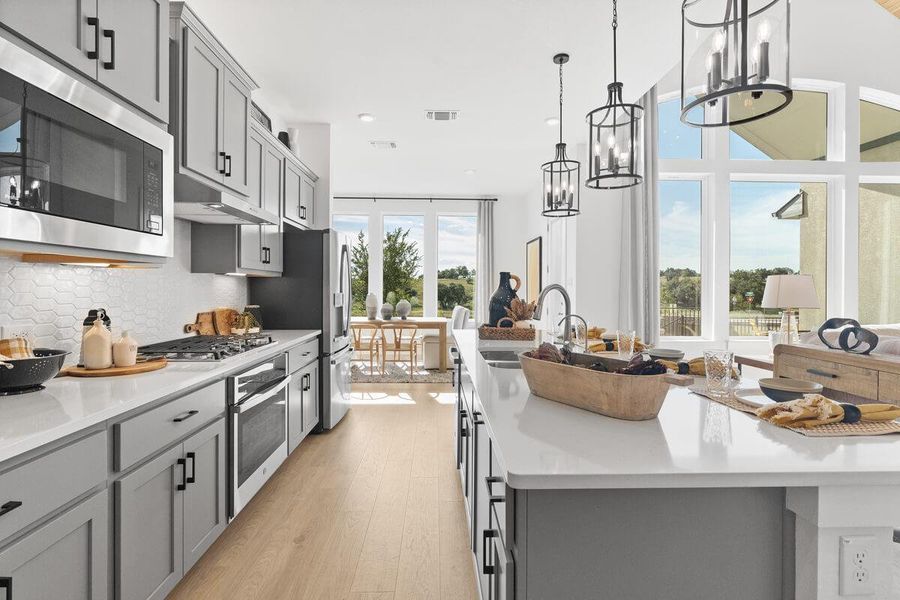 Kitchen featuring gray cabinets, stainless steel appliances, light wood finished floors, a large island with sink, and backsplash