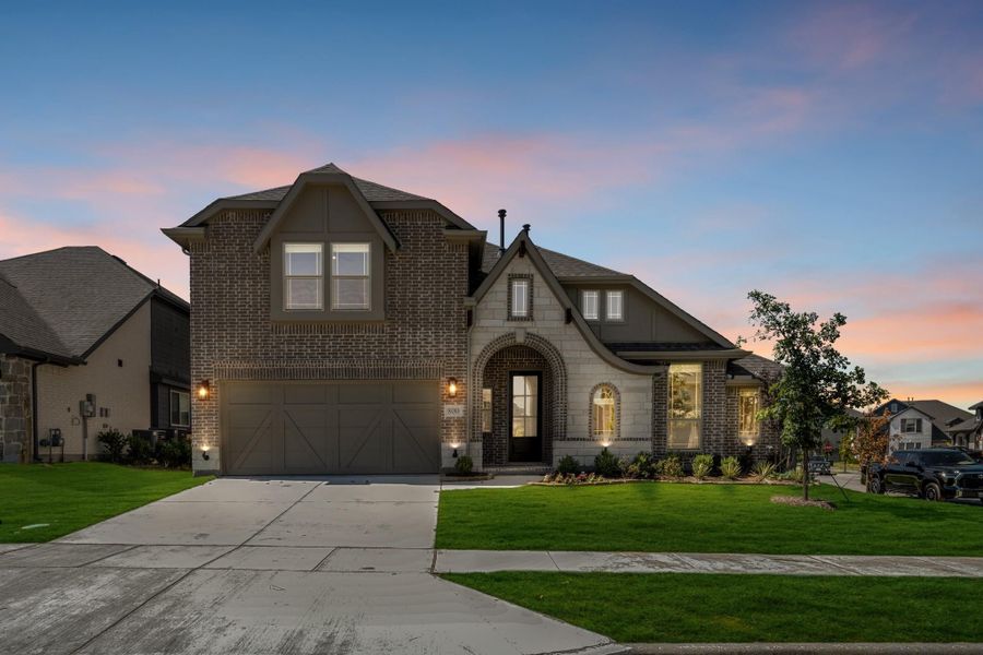 Two-story brick home with arched entry, two-car garage, and manicured lawn at dusk