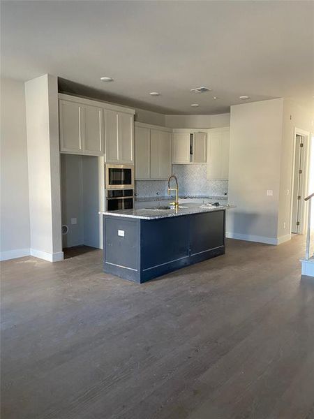 Kitchen with wood-type flooring, a center island with sink, stainless steel appliances, backsplash, and white cabinets