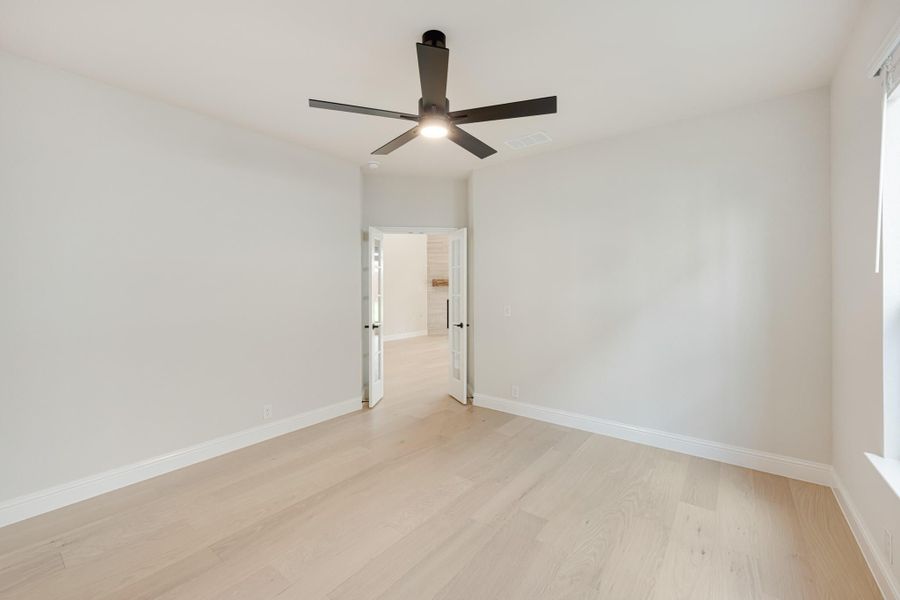 Empty bedroom with light hardwood floors, white walls, and a black ceiling fan with light fixture. Empty bedroom with light hardwood floors, white walls, and a black ceiling fan with light fixture.