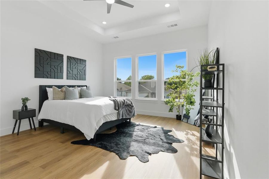 Bedroom with light wood-style floors, a ceiling fan, recessed lighting, and a raised ceiling