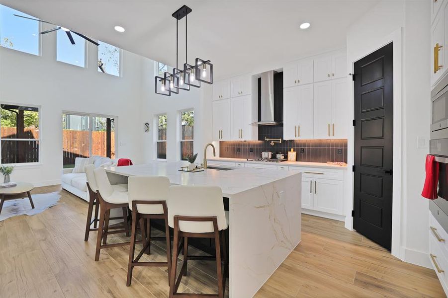 Kitchen featuring a wealth of natural light, wall chimney range hood, a center island with sink, light hardwood / wood-style flooring, and white cabinetry