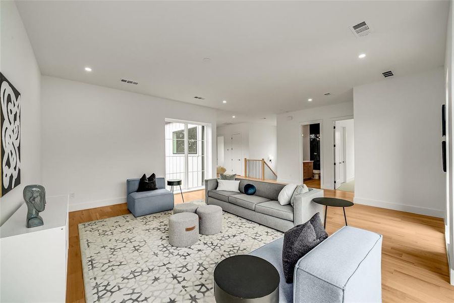 Spacious living area featuring light wood-finish flooring, recessed lighting, and white walls