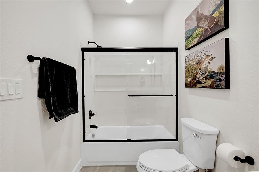 Bathroom featuring tile patterned floors, toilet, and enclosed tub / shower combo