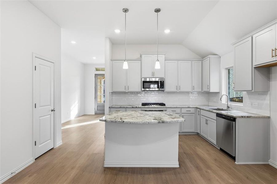 Kitchen with backsplash, stainless steel appliances, light stone countertops, a kitchen island, and light wood-type flooring Kitchen with backsplash, stainless steel appliances, light stone countertops, a kitchen island, and light wood-type flooring