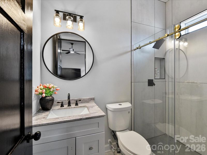 Modern ensuite bathroom with a sleek vanity, round mirror, and a glass-enclosed shower with stylish tile finishes.