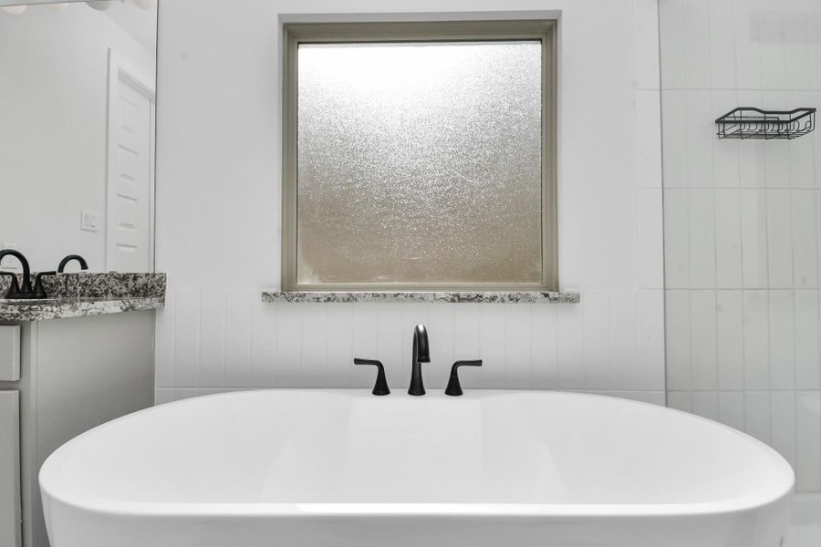 This bathroom features a modern freestanding bathtub with sleek black fixtures, a frosted window for privacy, and a stylish granite countertop. The space is bright and contemporary, offering a tranquil retreat. This bathroom features a modern freestanding bathtub with sleek black fixtures, a frosted window for privacy, and a stylish granite countertop. The space is bright and contemporary, offering a tranquil retreat.