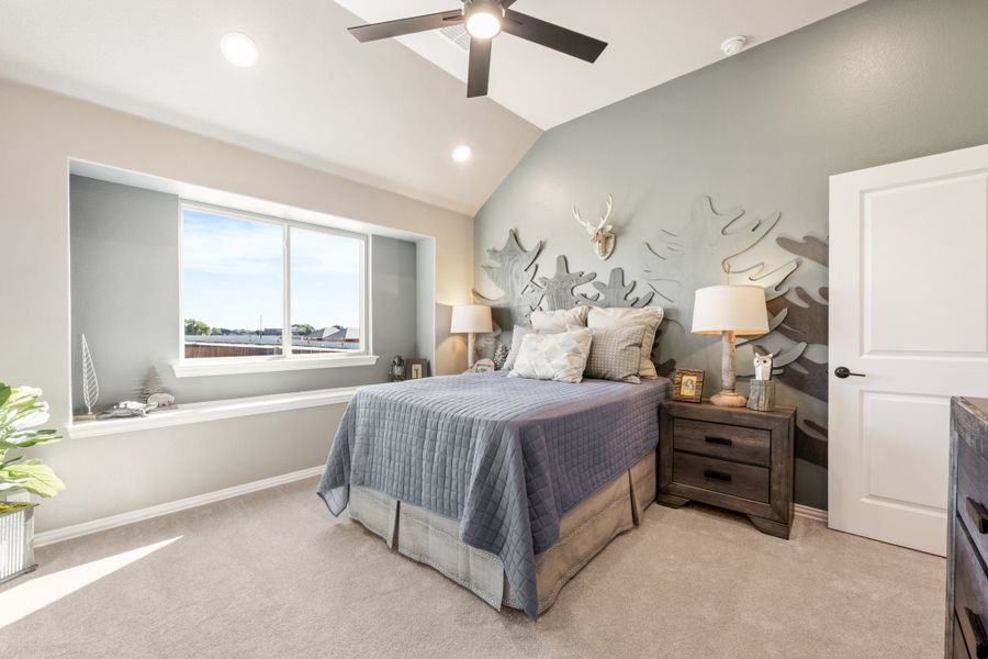Bedroom with vaulted ceiling, ceiling fan, accent wall, and large window with natural light